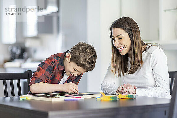 Lächelnde Mutter betrachtet ihren Sohn beim Zeichnen auf einer Schiefertafel in der Küche