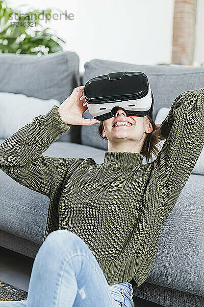 Lächelnde Frau im Pullover mit Virtual-Reality-Headset zu Hause