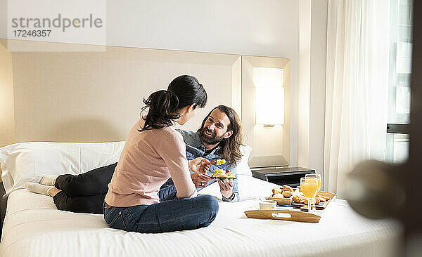 Lächelnder Mann sieht Frau beim Frühstück im Bett an