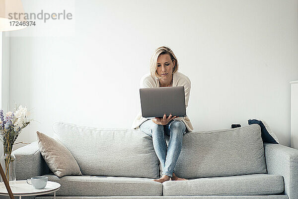 Mittlere erwachsene Frau mit Laptop auf dem Sofa zu Hause