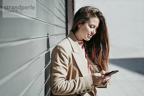 Junge Frau  die an einem sonnigen Tag ein Mobiltelefon mit einem Rollladen benutzt