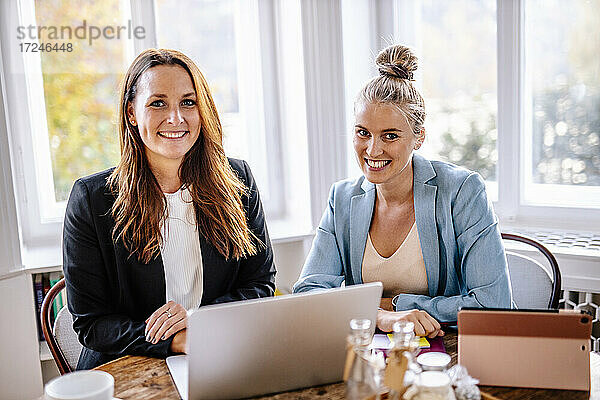 Glückliche Unternehmerinnen sitzen mit Laptop im Büro