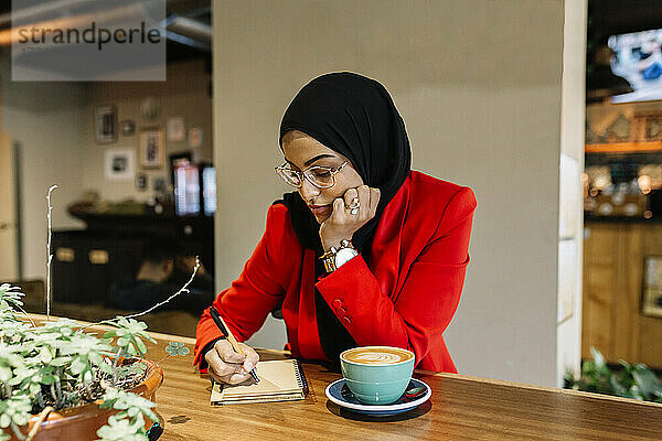 Junge Geschäftsfrau schreibt in einem Café in ihr Tagebuch