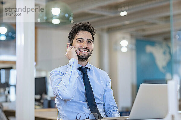 Junger Geschäftsmann schaut weg  während er im Büro mit dem Handy telefoniert