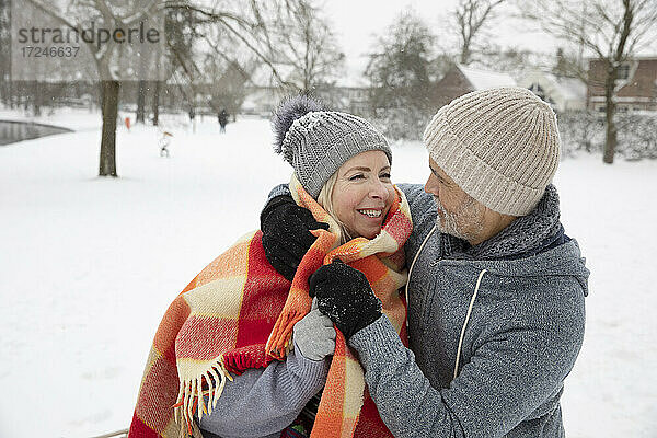 Mann wickelt Frau mit Decke im Winter ein