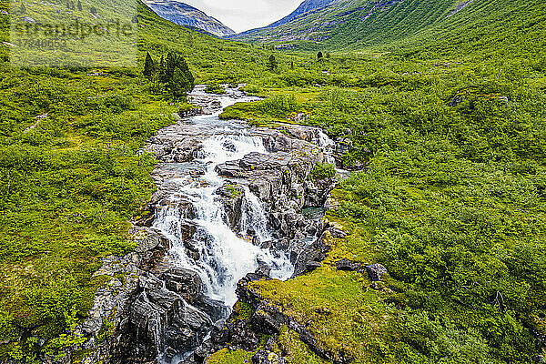 Wasserfall  der durch Felsen in einem grünen Bergtal fließt