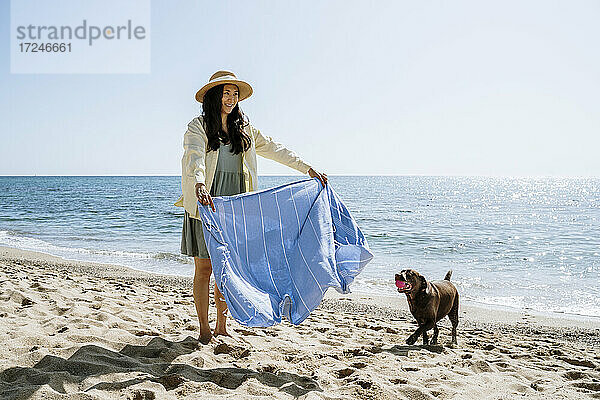 Lächelnde Frau  die ein Tuch an einem Hund im Sand am Strand hält
