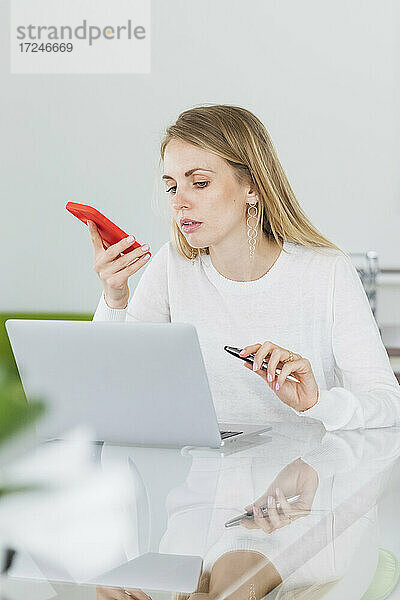 Unternehmerin sendet Sprachnachricht  während sie im Büro auf den Laptop schaut