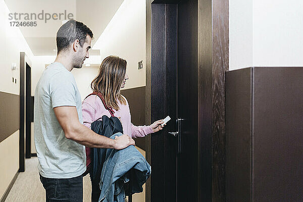 Frau benutzt Kartenschlüssel zum Aufschließen der Tür  während sie neben einem Mann im Hotel steht