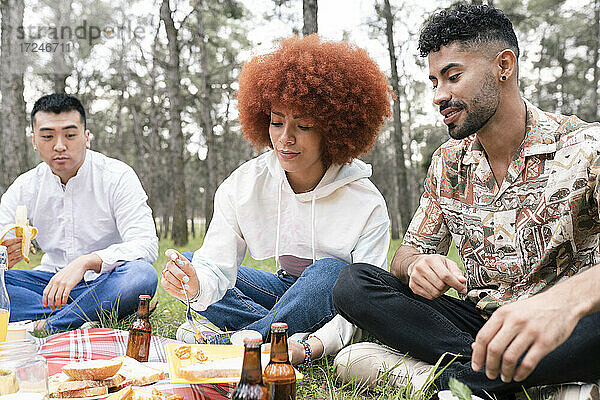 Männliche und weibliche Freunde essen Essen während einer Party im Wald