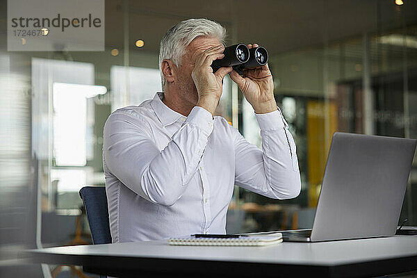 Unternehmer  der ein Fernglas benutzt  während er im Büro sitzt