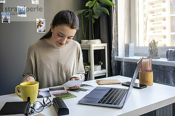Junge Frau überprüft ein Foto  während sie zu Hause am Laptop sitzt