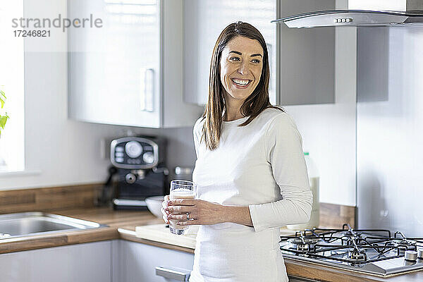 Lächelnde Frau schaut weg  während sie ein Glas Milchshake in der Küche hält