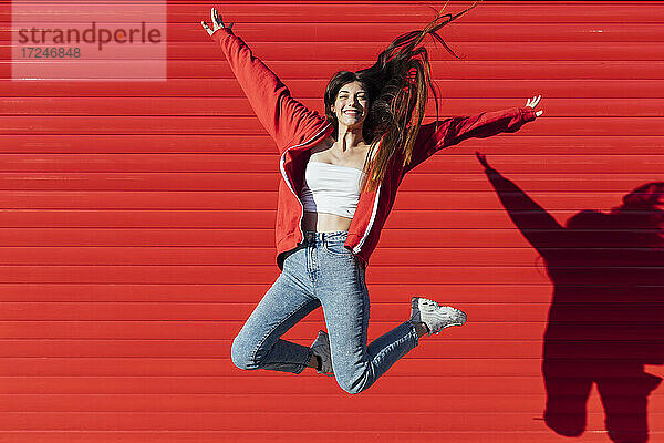 Teenager-Mädchen mit zerzaustem Haar springt vor einer roten Wand