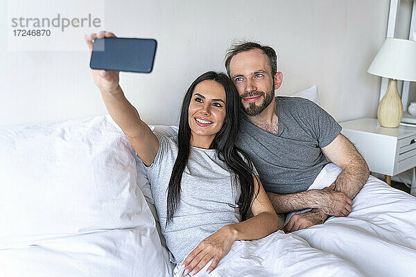 Frau nimmt Selfie mit Mann durch Smartphone auf Bett zu Hause