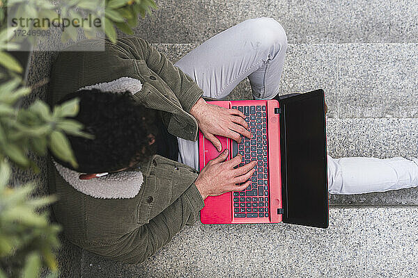 Mann tippt auf Laptop  während er auf Stufen sitzt