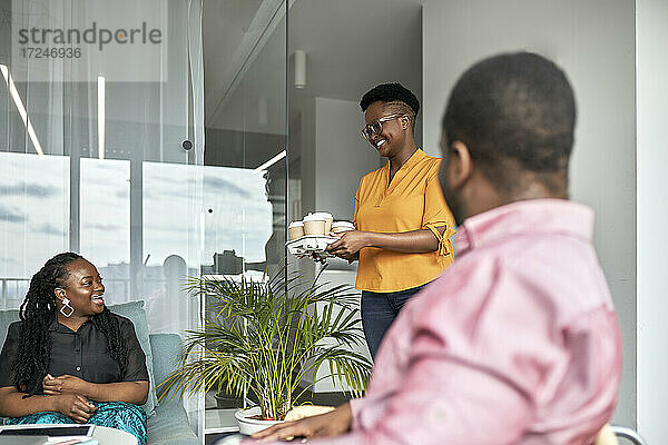 Lächelnde Geschäftsfrau  die männlichen und weiblichen Mitarbeitern im Büro Kaffee anbietet