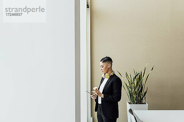 Berufstätige Frau mit Einweg-Kaffeebecher und digitalem Tablet im Büro
