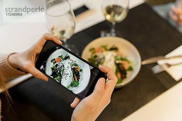 Frau fotografiert Essen im Restaurant mit ihrem Smartphone