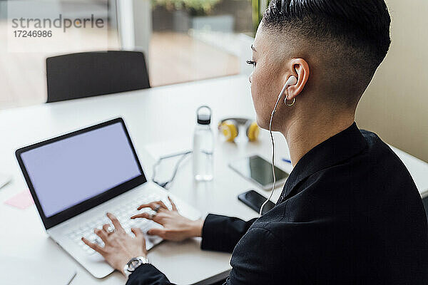 Junge Geschäftsfrau mit In-Ear-Kopfhörern bei der Arbeit am Laptop im Büro