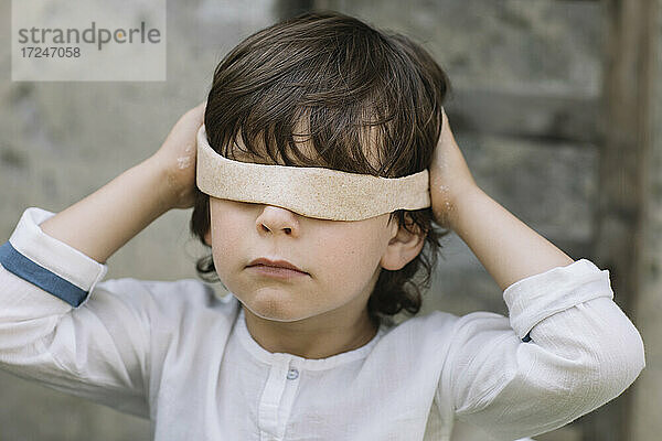Unschuldiger Junge  der sich beim Spielen im Hinterhof die Augen mit Knete verdeckt