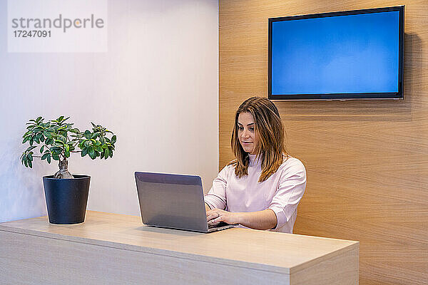 Weibliche Empfangsdame arbeitet am Laptop am Schreibtisch in einer Klinik