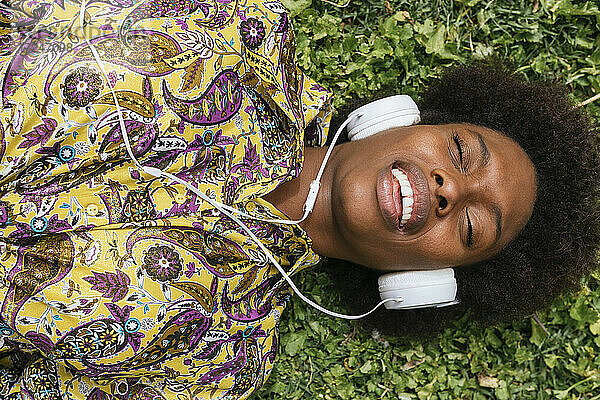 Schöne Frau mit Kopfhörern  die lächelnd im Gras liegt
