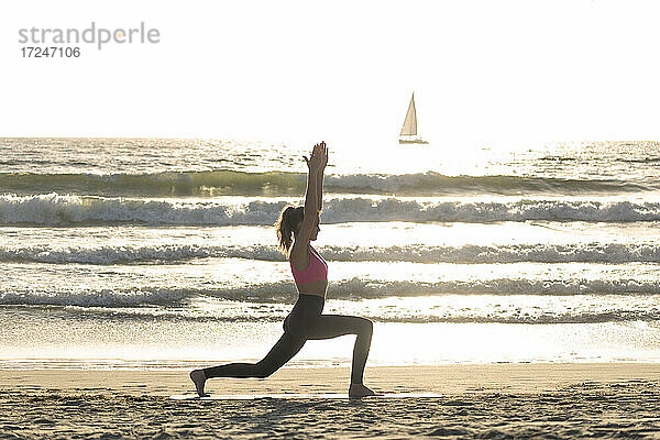 Frau übt Yoga am Meeresufer an einem sonnigen Tag
