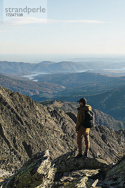 Mann mit Rucksack  der auf einem Felsen stehend den Berg betrachtet  während er im Urlaub ist