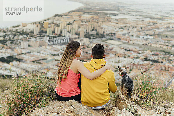 Paar sitzt mit Hund auf einem Hügel