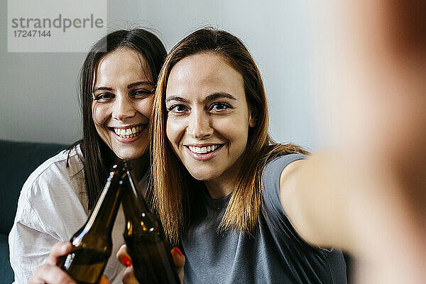 Glückliche junge Frauen machen ein Selfie und stoßen mit Bierflaschen an