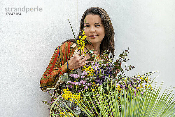 Lächelnde Frau mit Blumenstrauß vor einer weißen Wand stehend