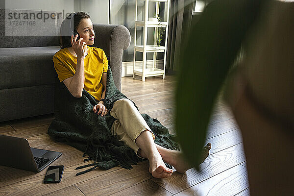 Frau hört Musik über Kopfhörer  während sie zu Hause an einem Laptop und einem Mobiltelefon sitzt