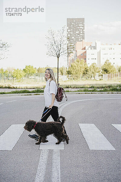 Lächelnde Frau mit Hund beim Überqueren der Straße in der Stadt