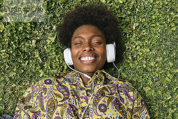 Lächelnde Frau hört Musik über Kopfhörer  während sie im Gras liegt
