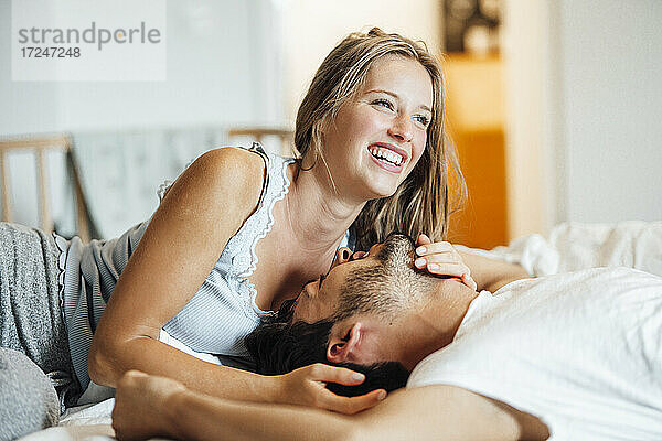 Fröhliches junges Paar liegt zu Hause auf dem Bett