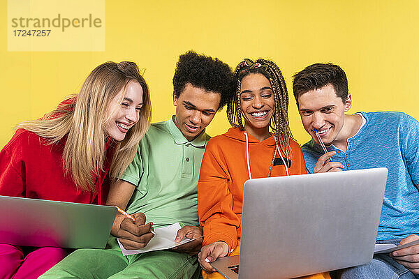 Lächelnde Freunde studieren gemeinsam an einem Laptop vor einem gelben Hintergrund