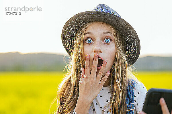 Schockiertes blondes Mädchen mit Hut auf einem landwirtschaftlichen Feld