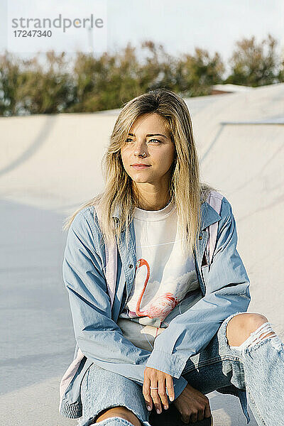 Schöne Frau schaut weg  während sie in einem Skateboardpark sitzt