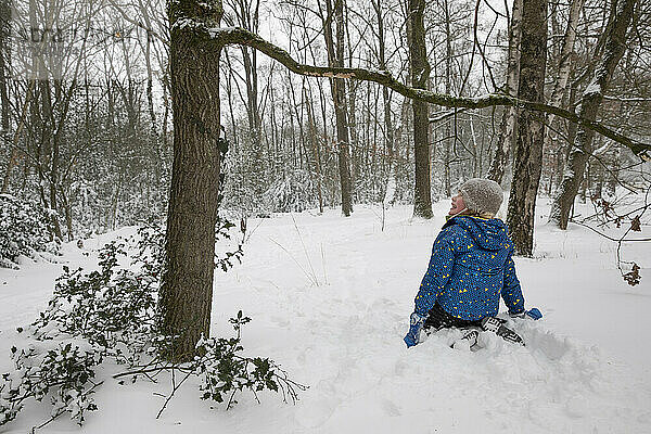 Junge schaut weg  während er im Winter in der Nähe eines Baumes im Schnee kniet