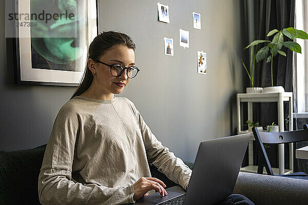 Junge Frau mit Brille arbeitet zu Hause am Laptop
