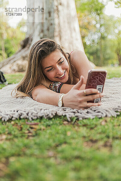 Lächelnde Frau nimmt Selfie durch Handy in öffentlichen Park
