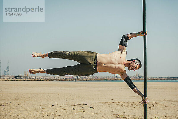 Männlicher Sportler bei einer Übung  während er am Strand auf einer Stange balanciert