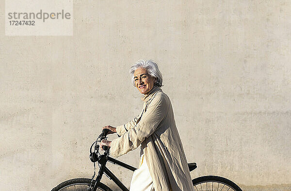Lächelnde reife Frau auf Fahrrad an der Wand