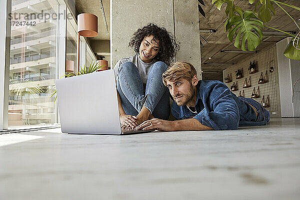Mann benutzt Laptop mit Freundin auf dem Boden seiner Wohnung