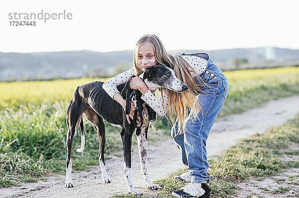 Blondes Mädchen umarmt Hund auf dem Fußweg