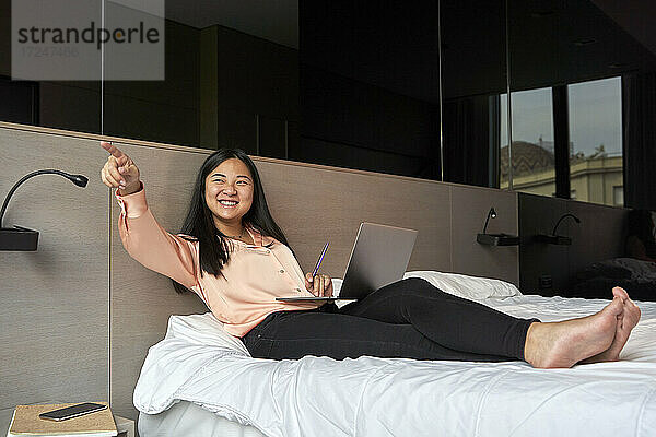 Lächelnde weibliche Fachkraft  die mit einem Laptop im Hotel sitzt und darauf zeigt