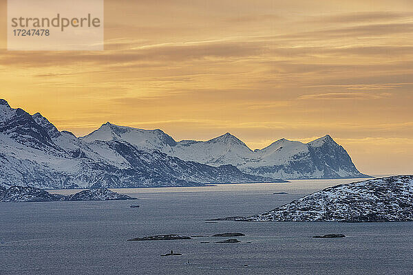 Norwegen  Tromso  Kvaloya  Dramatischer Himmel über dem schneebedeckten Berg Senja Island von der Insel Kvaloya aus gesehen bei Sonnenuntergang