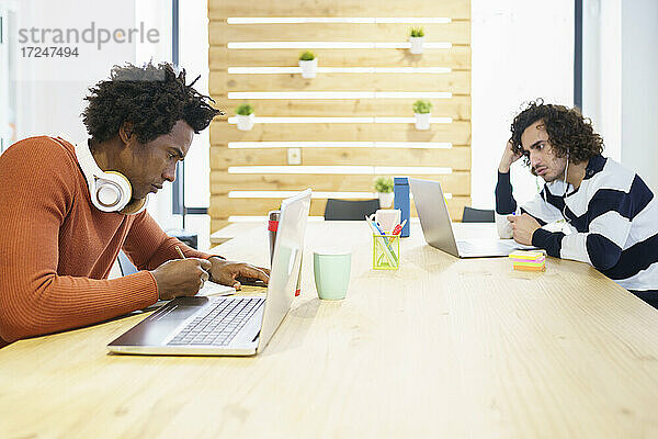 Multiethnische männliche Mitarbeiter  die im Büro sitzend einen Laptop benutzen