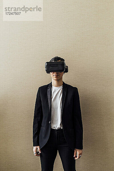 Junger Berufstätiger mit Virtual-Reality-Simulator vor einer Wand im Büro